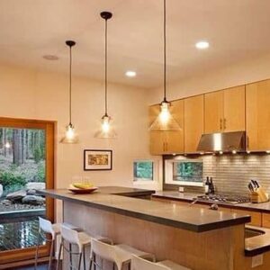 Heidi Transparent Glass Funnel Pendant Light - A modern kitchen with three glass pendant lights hanging over a kitchen island. The kitchen features wooden cabinets, a stainless steel range hood, and large windows overlooking a forest.
