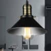Agda Loft Black English Street Style Pendant Light - A vintage-style pendant light with a black metal shade and a brass fitting. The light is hanging from a ceiling and illuminating a room with a wooden table and bookshelves.