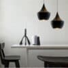 Judit Arabic Inspired Pendant Light - Two black, conical pendant lights hang above a minimalist dining table. The lights cast a warm glow on the table and chairs.