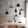 Judit Arabic Inspired Pendant Light - A cluster of black, conical pendant lights hangs over a dining table in a minimalist interior. The lights cast warm, ambient light on the table and chairs.