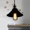 Agda Loft Black English Street Style Pendant Light - A vintage-inspired pendant light with a black metal shade and a brass fitting. The light is illuminated by an Edison-style bulb and hangs above a wooden shelf with towels.