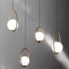 Insuppar Oval Ring Ball Pendant Light - Four modern pendant lights with a circular design. Each light has a white glass globe enclosed within a gold metal ring. The lights are hanging from black cords against a gray background.
