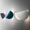 Oysteu Modern Minimalist Shell Wall Light - Three modern wall sconces in different sizes and colors, mounted on a white wall. The sconces have a geometric, folded paper-like design, with one in white, one in blue, and one in black.