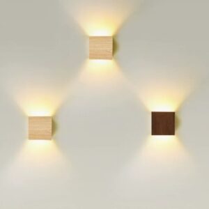 Cabanori Scandinavian Wooden Vibes Cube Wall Light - Three wooden wall sconces mounted on a white wall, each emitting a warm, ambient light. The sconces are in different wood tones: light wood, medium wood, and dark wood.